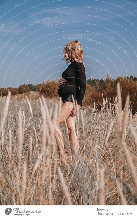 Young, blond pregnant woman on the beach bent grass wearing black bodysuit holding pregnancy belly. Free space. Maternity. Summer pregnancy concept. abdomen
