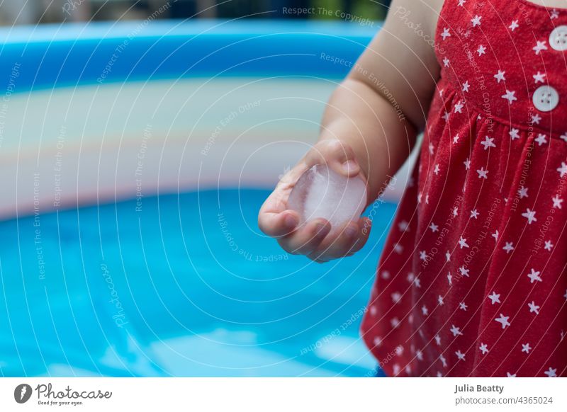 One year old baby doing a sensory play activity with ice cubes in an inflatable pool in the summer touch hold cold child experience learn grow try hands on