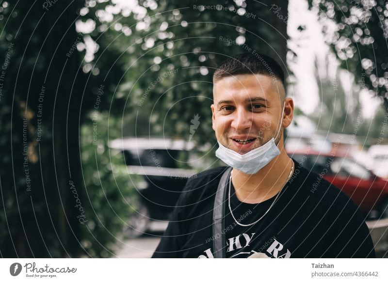 young man with fashion haircut , with a medical mask removed from his face and smiles. Close up portrait coronavirus joy pandemic quarantine success happy