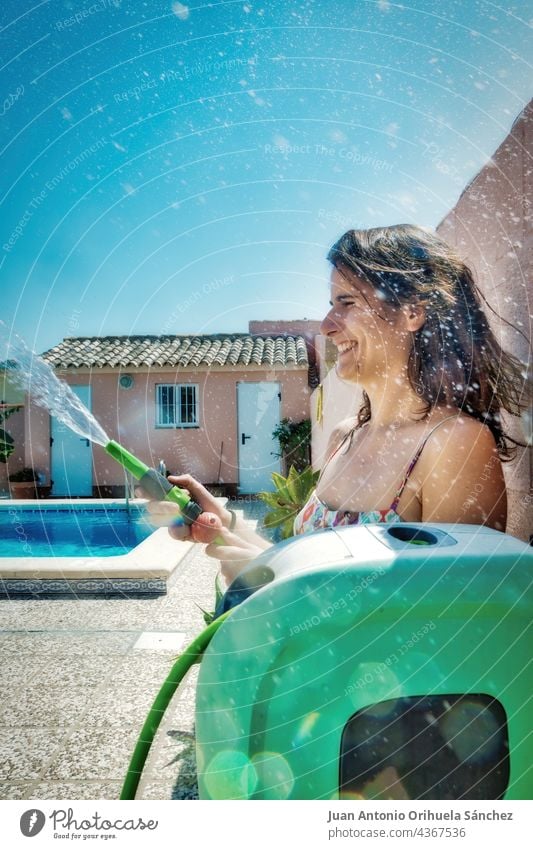 Pretty girl has fun throwing water with a hose. pretty wet splash house drops sunny season summer splashing refreshing happy laugh smile sexy home laughing