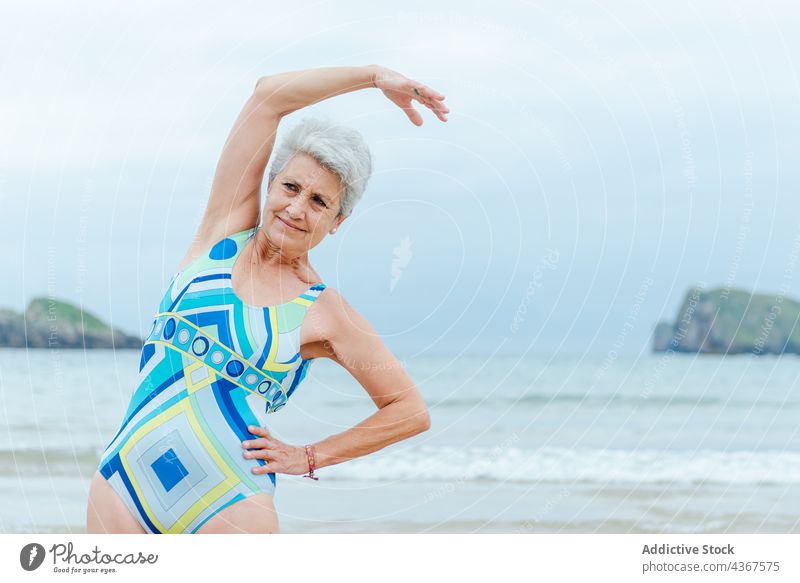 Old woman doing exercises on beach senior workout healthy lifestyle positive swimsuit sea activity female gray hair old ocean colorful swimwear beachwear