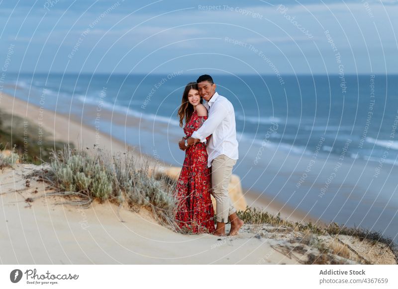 Gentle multiethnic couple standing on hill near sea at evening embrace summer elegant romantic love together hug multiracial diverse black african american