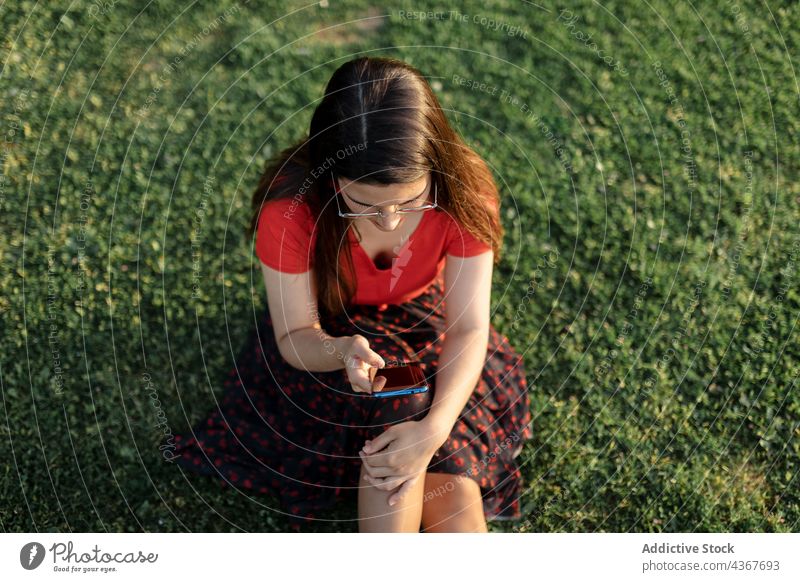 Woman browsing smartphone on lawn in park woman weekend summer evening entertain message using female surfing relax connection device sit meadow internet
