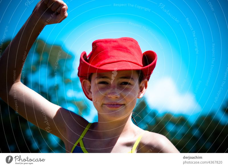 This is what winners look like. Young girl with red hat, stretches her right hand upwards. In the background blue sky and small white clouds. Colour photo