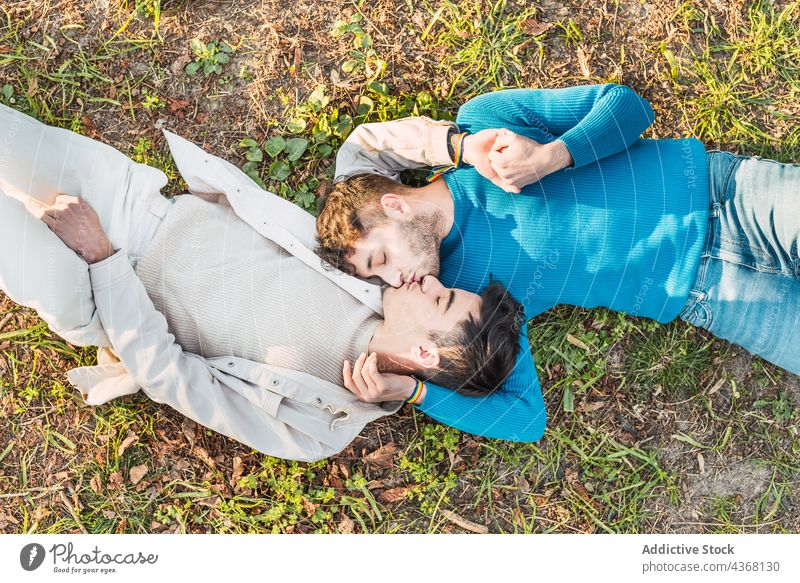 Smiling gay couple lying on lawn in park and kissing men grass face to face love homosexual male smile together relationship happy relax nature romantic