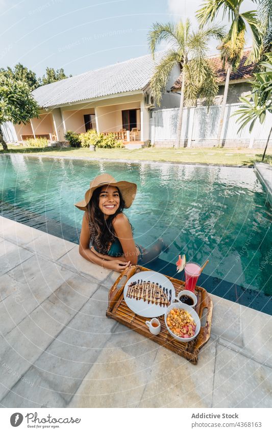 Content traveler in pool against tasty breakfast in summer resort vacation journey smile woman portrait coffee tropical tourist tray cheerful water poolside