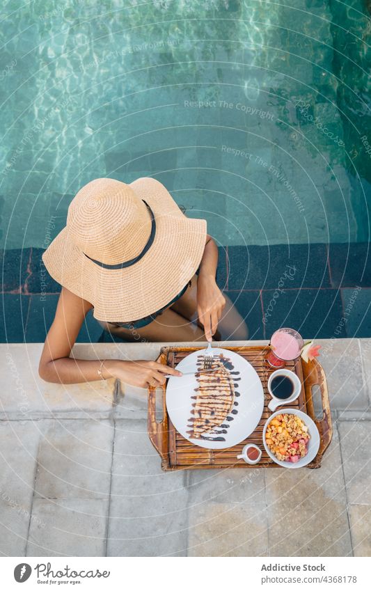 Unrecognizable traveler in pool cutting crepe during breakfast outdoors tourist power bowl resort delicious sweet woman coffee vacation knife chocolate sauce