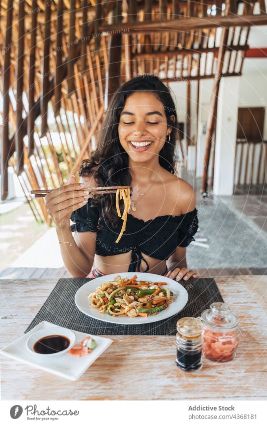 Smiling traveler with noodles between chopsticks in restaurant asian food cheerful lunch meal table woman enjoy smile food stick vegetable nutrition delicious