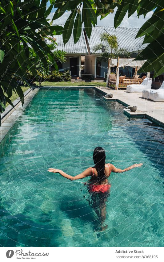 Unrecognizable traveler swimming in pool in tropical resort vacation tourism exotic woman summer swimsuit tourist nature architecture house ripple tree water