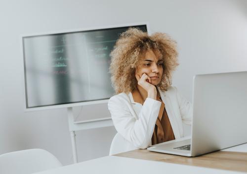Young curly hair woman working on laptop in bright office with big screen behind her adult attractive beautiful black business caucasian communication computer