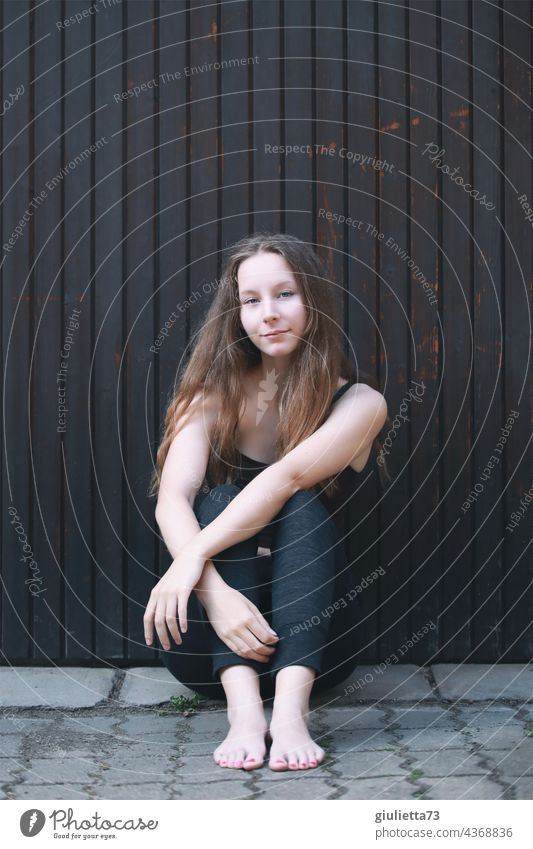 Portrait of teenage girl with long hair, cool, smiling, sitting on the ground outside Exterior shot Looking into the camera portrait teenager