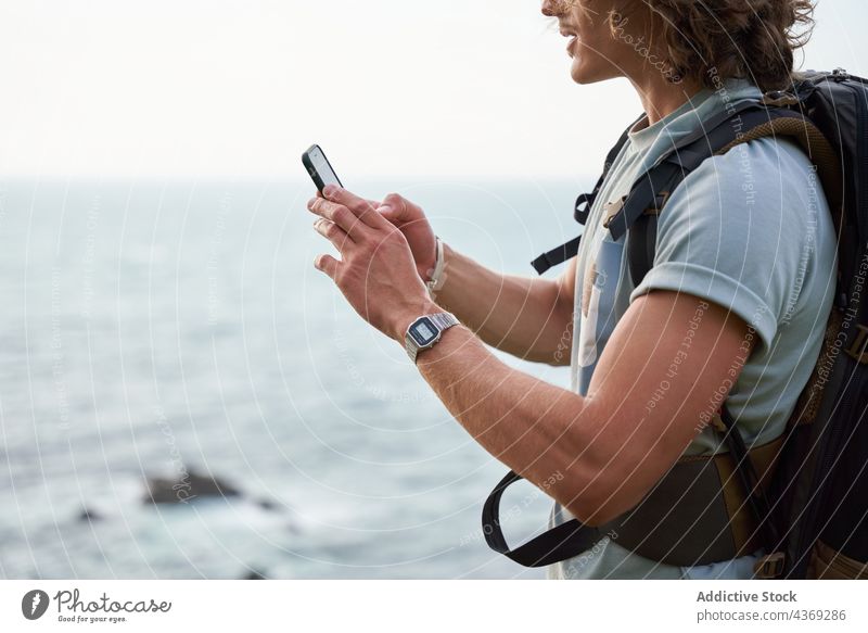 Traveling man browsing phone on hill against sea watching texting smartphone traveler trekking cheerful hiker summer take photo male nature gadget using