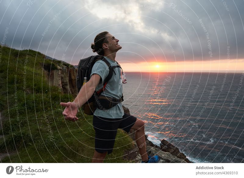 Traveling man enjoying freedom with outstretched arms on rock hiker carefree viewpoint mountain sunset male edge rocky stand sea nature water adventure travel