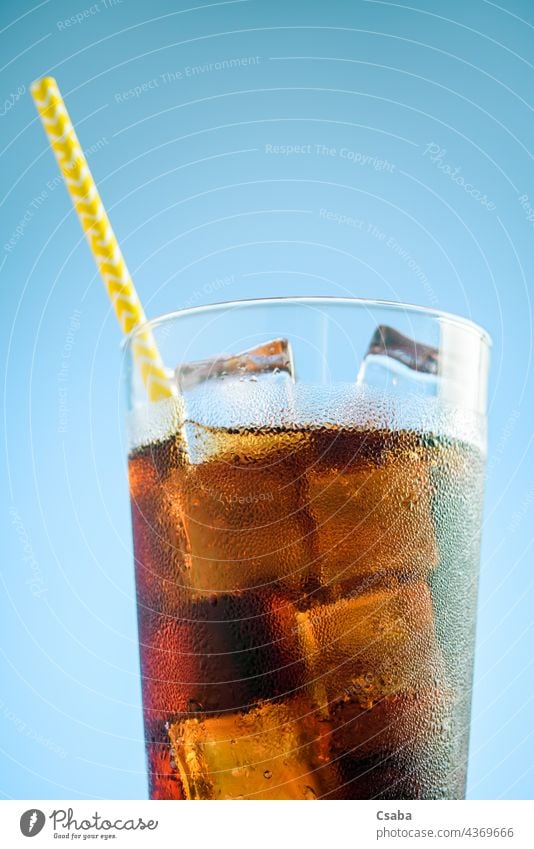 A glass of cola with ice on blue and pink background soda soft drink cold straw summer refreshment caffeine liquid brown beverage condensation dew cube
