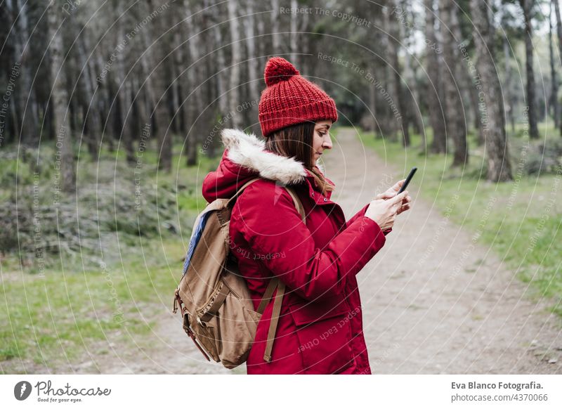 side view of backpacker caucasian woman walking in forest using mobile phone during winter or autumn season. Lifestyle and nature. Wide angle view technology