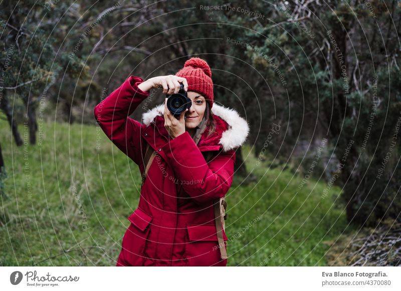 backpacker caucasian woman taking picture with camera in forest during winter or autumn season. Lifestyle and nature reflex photographer hiking mountain cold
