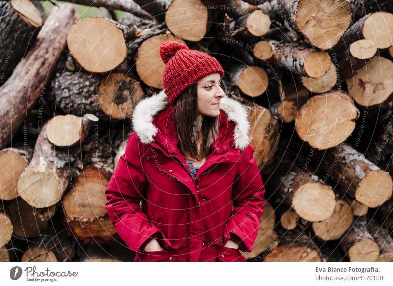 relaxed caucasian woman standing in front on wood trunks in mountain during autumn or winter season. Lifestyle and nature forest cold trip red hat coat enjoy