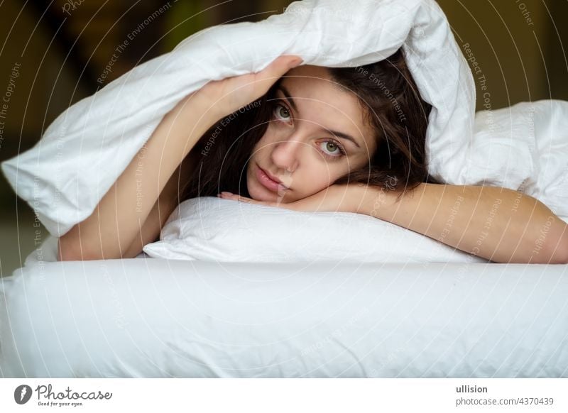 Portrait of an attractive, young, sexy brown haired woman in Bed, hand and head on the pillow under the blanket, Copy space. lifestyle resting pretty bedding