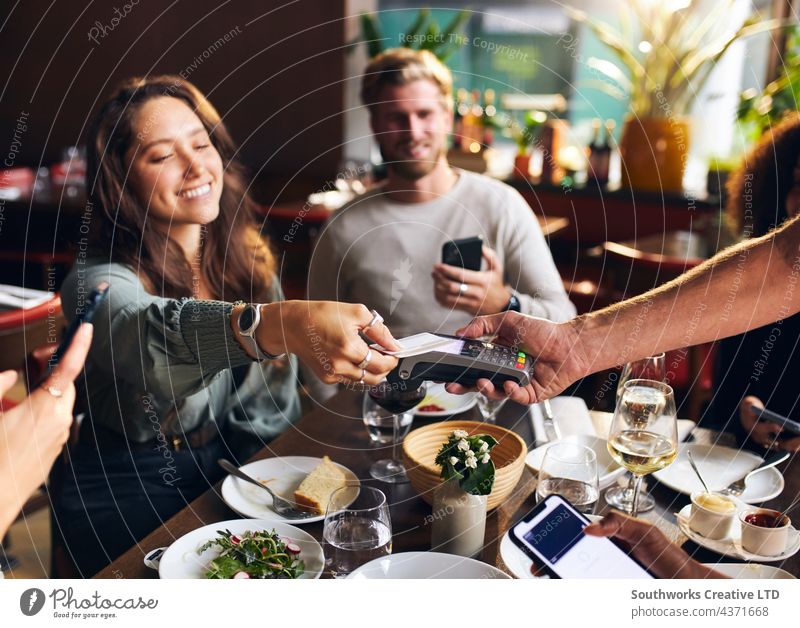 Woman paying with card in restaurant woman contactless young bill technology connection indoors day venue interior group three caucasian people candid smiling