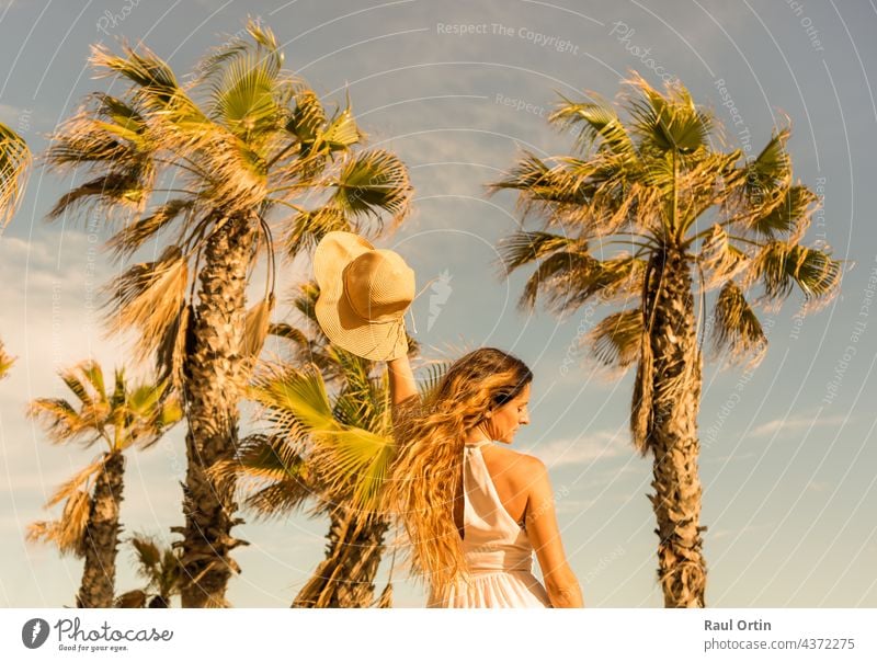 Portrait beautiful woman dancing holding sunhat on beach palm trees background.Summer holidays concept lifestyle dance dress white summer fashion person sand