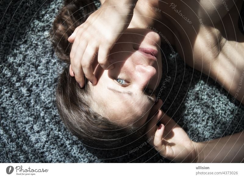 Portrait of a beautiful young attractive sexy woman, lying on carpet, partially with shadows of a string curtain Woman portrait decorative calm sunlight
