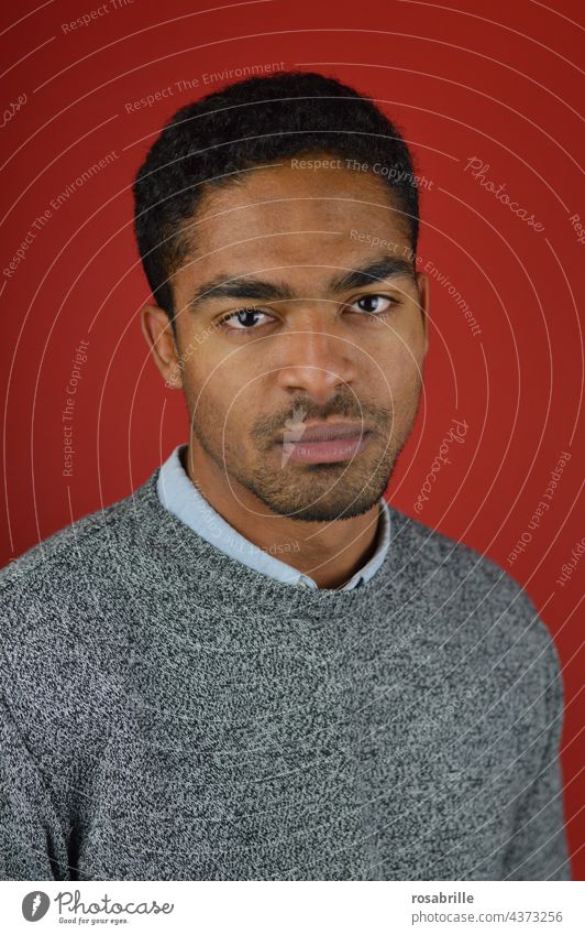 young man looks seriously into the camera in front of a red background Man youthful multiracial Caucasian-African portrait Human being Masculine Young man Red