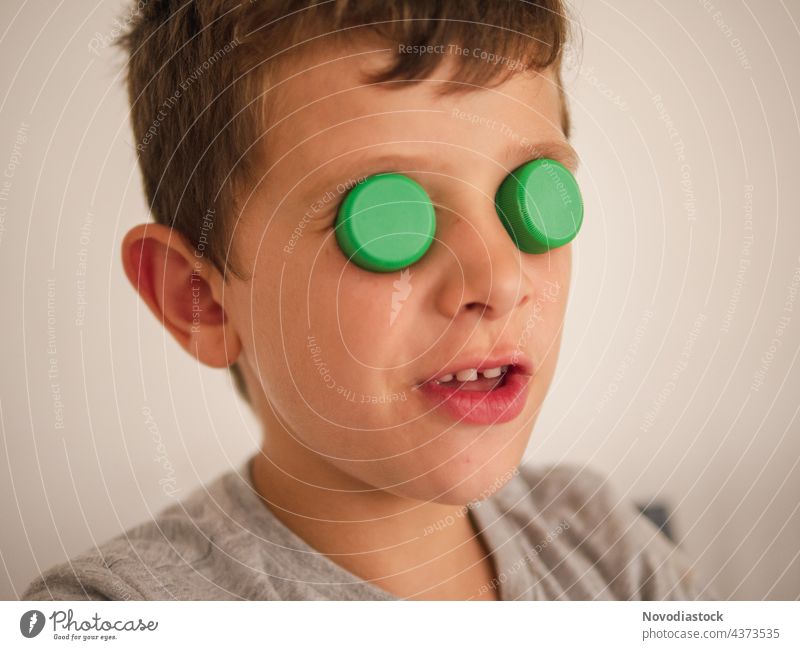 Young boy with plastic lids on his eyes cap top funny covered portrait close up caucasian enjoyment gesture expression casual child young home indoors bottle