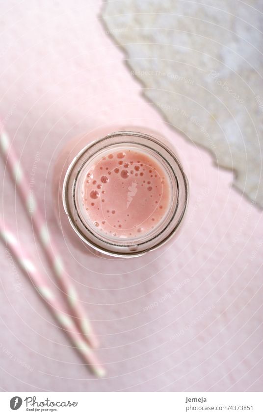 Strawberry smoothie in a botle with pink background and pink paper straws. milkshake healthy strawberry detox glass fruit yogurt dairy cold vertical high angle