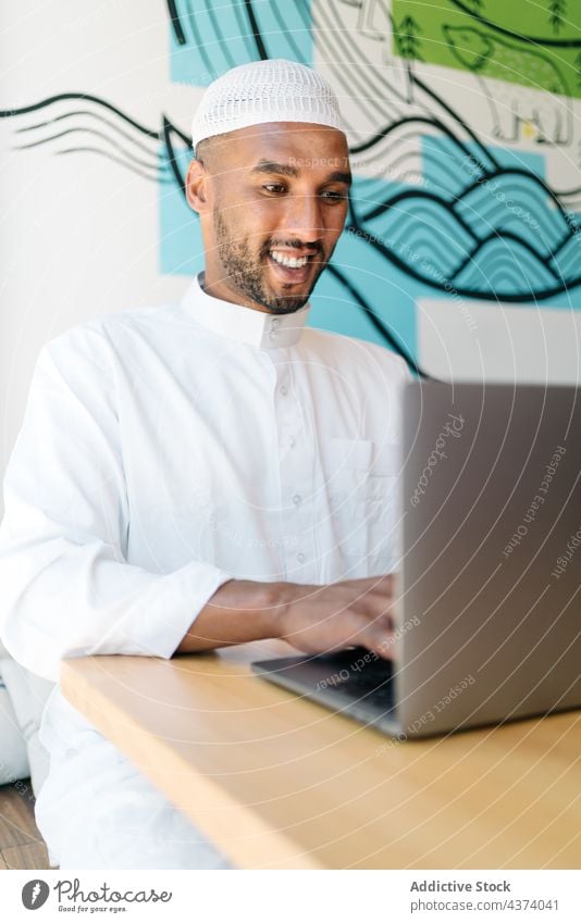 Islamic man using laptop in cafe smile rest weekend social media typing authentic male freelance data browsing device gadget cheerful netbook ethnic muslim