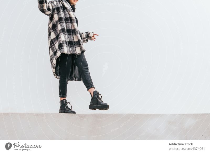 Crop stylish female walking on border woman balance street wall exterior style weekend rest trendy urban outfit city modern fashion casual coat checkered