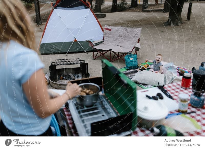 baby sitting on the ground at a tent campsite while mom cooks on a camp stove blonde california camper camping caucasian chair child childhood cooking daughter