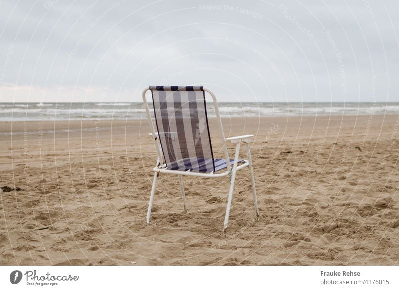 Blue and white folding chair on the beach overlooking the North Sea Folding chair Beach White Striped sea view Ocean Camping chair on one's own forsake sb./sth.