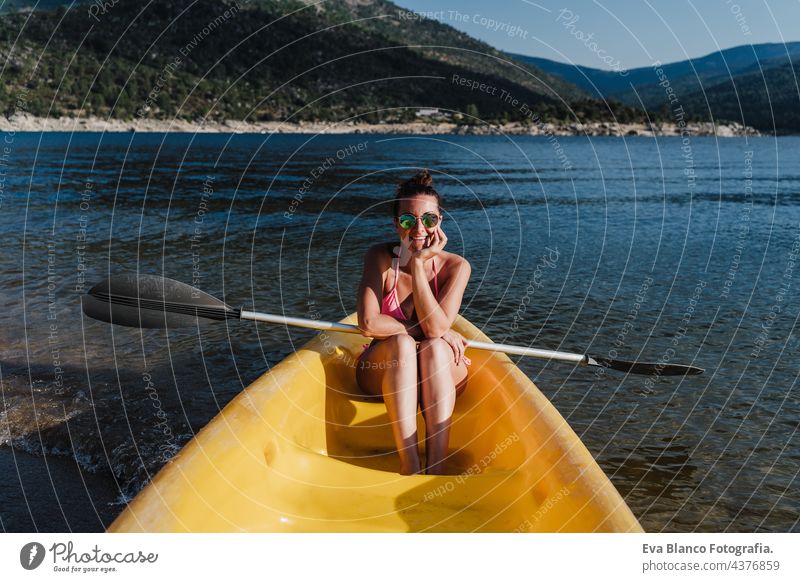 smiling caucasian woman in swim wear holding oar sitting on yellow canoe in lake during sunny day. summer time. Sports, adventure and nature rowing happy sports