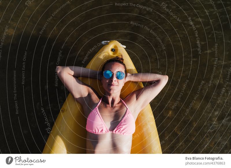 top view of happy caucasian woman lying on yellow canoe in lake during sunny day. summer time. Sports, adventure and nature. Woman in swim wear and sunglasses