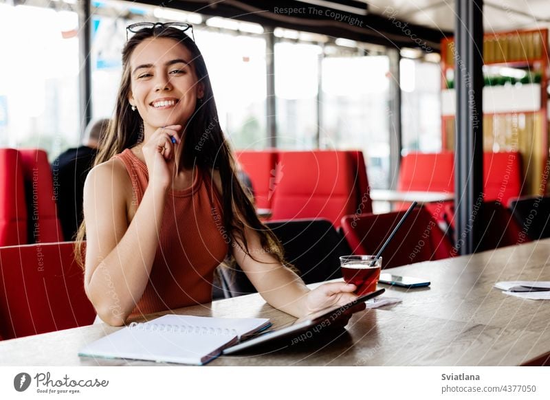 A beautiful girl with a notebook and a tablet is sitting in a cafe and studying or working notepad student freelancer break education learning writing business