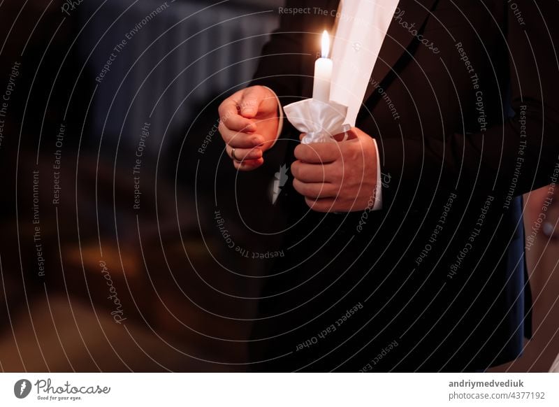 Couple in church. groom hold shiny candles during the ceremony in church. Hands of newlywed with candle in church. Church religious details. Newlyweds swear to each other to love forever.