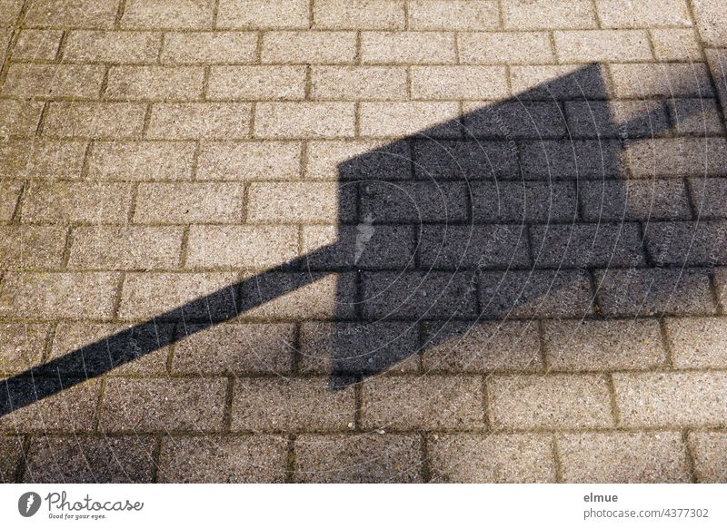 The shadow from the timetable notice on a bus stop sign falls on the grey cobblestones of the pavement Paving stone off Shadow Timetable Bus stop Lanes & trails