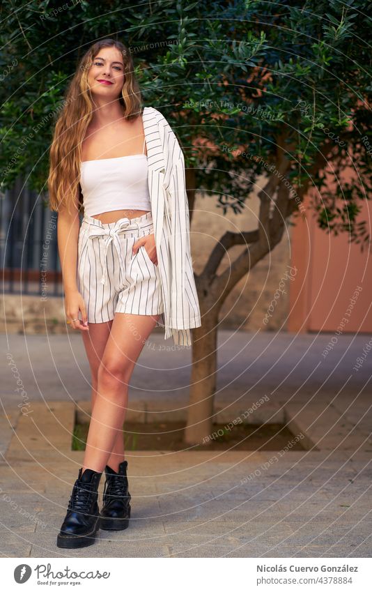 Fashionable and stylish young woman posing on an urban street. Smart clothes, white and black striped, white top and she is carrying her jacket on the shoulder.