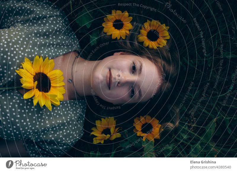 Portrait of a young girl lying on the grass among flowers. Top view. portrait sunflower dress summer beautiful femininity top view smile blond hair chain
