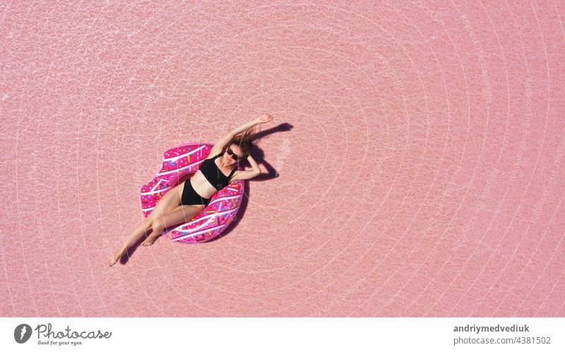 Aerial view of Beautiful woman lying in a bikini on inflatable mattress on pink salt lake. copy space. opening of the tourist season. summer holiday concept. taken from above from a drone