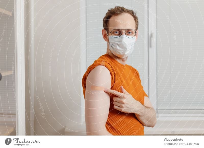 young caucasian man holding up shirt sleeve to show the sticking plaster after a covid-19 jab in shoulder arm vaccine vaccination injection disease adult health