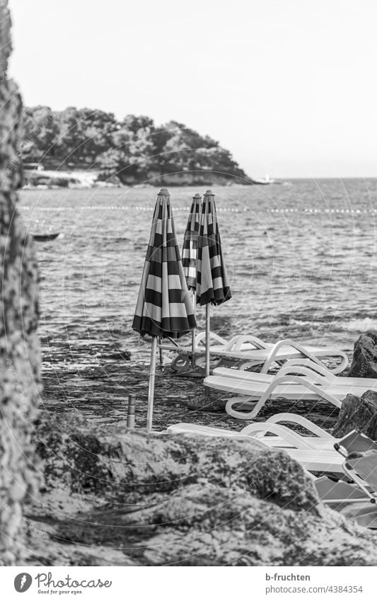 closed umbrellas on the beach parasols Ocean Closed sun lounger Beach Rock Croatia Water Black & white photo Morning Bay on one's own Loneliness