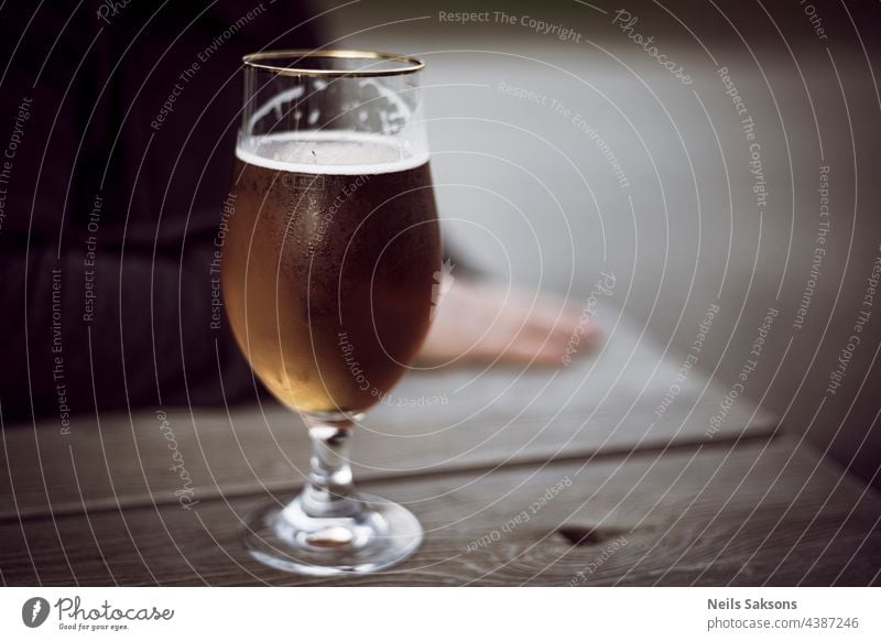 glass of beer with dew on wooden table. blurred human silhouette behind bar water drops fresh freshness alcohol beverages drink refreshment liquid restaurant