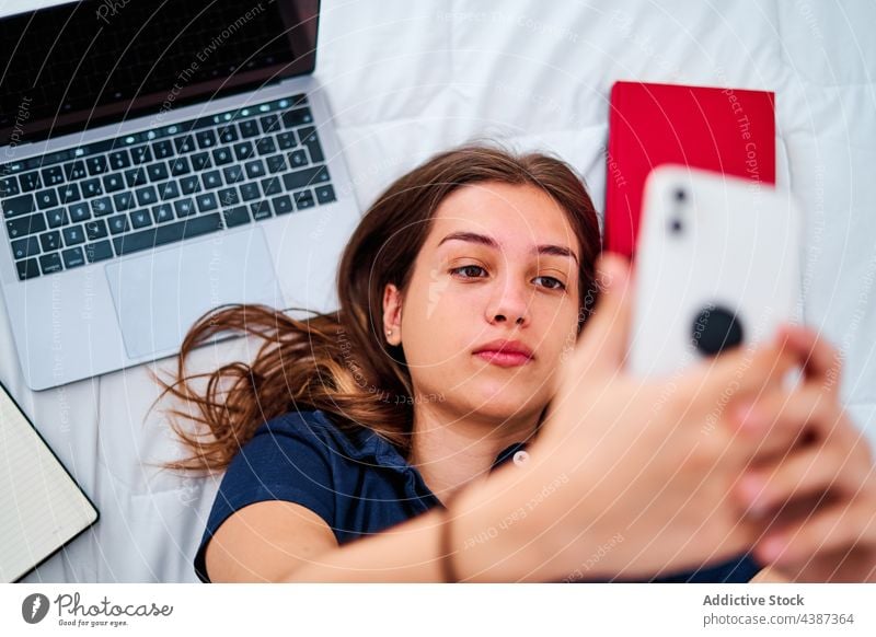 Female student taking selfie on smartphone woman at home online gadget bed break remote female young take photo device laptop mobile using internet education