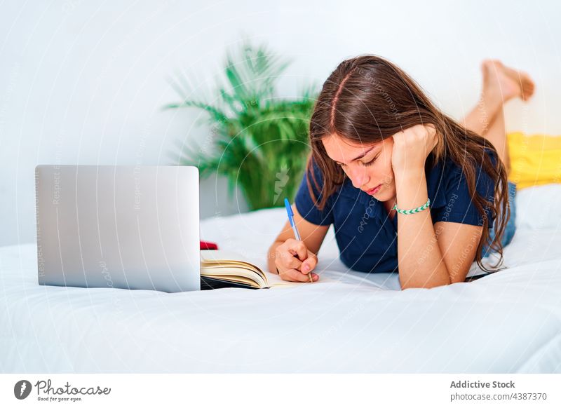 Young woman studying online in bedroom student write laptop at home remote education gadget female young teen teenage take note internet device smart assignment
