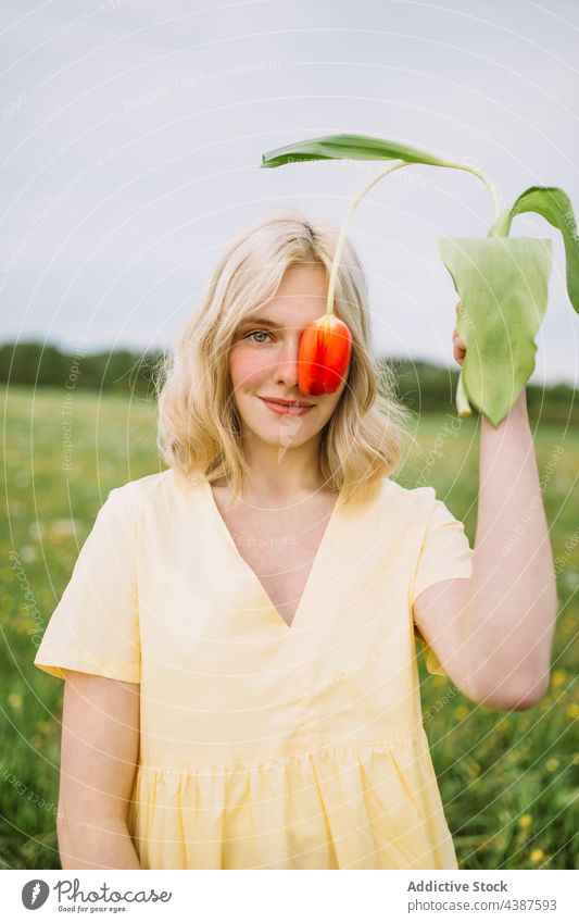 Smiling woman covering eye with red tulip in meadow cover eye flower field spring tender content floral female blossom bloom fresh natural summer calm delicate