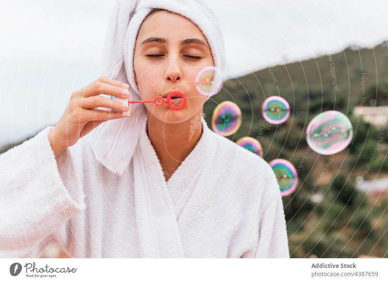 Young female blowing bubbles during skin care routine woman soap bubble balcony home weekend rest clean spa young air toy play hygiene terrace wellbeing