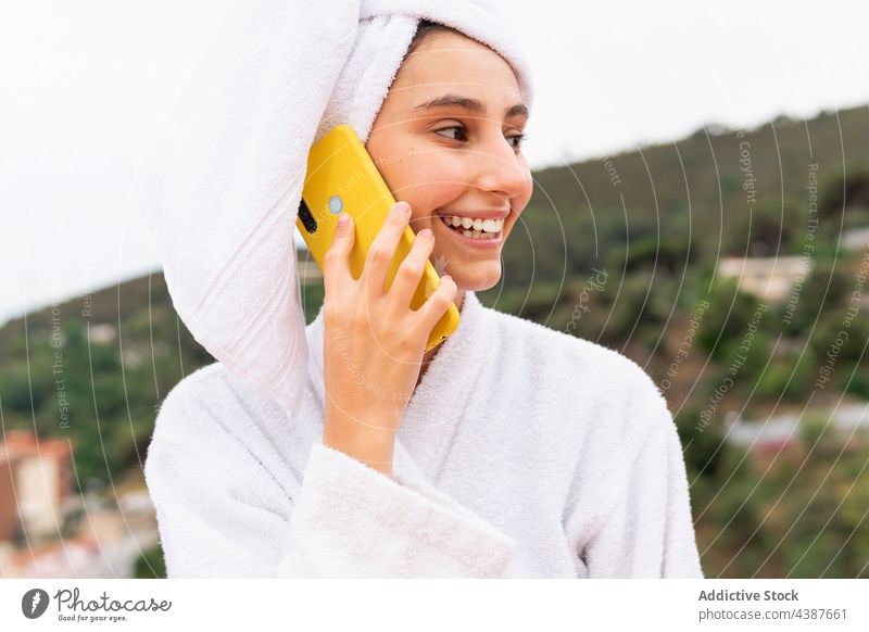 Woman using smartphone on balcony after shower woman skin care rest clean smile social media female weekend browsing towel bathrobe relax gadget device surfing