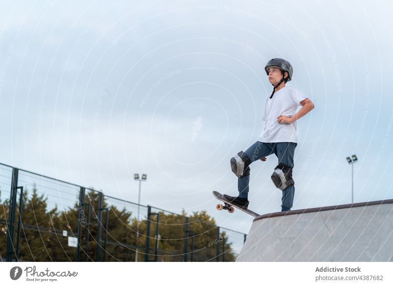Teen boy riding skateboard in skate park skater ride teenage activity skill energy stand hobby urban move hand on waist action active serious determine summer