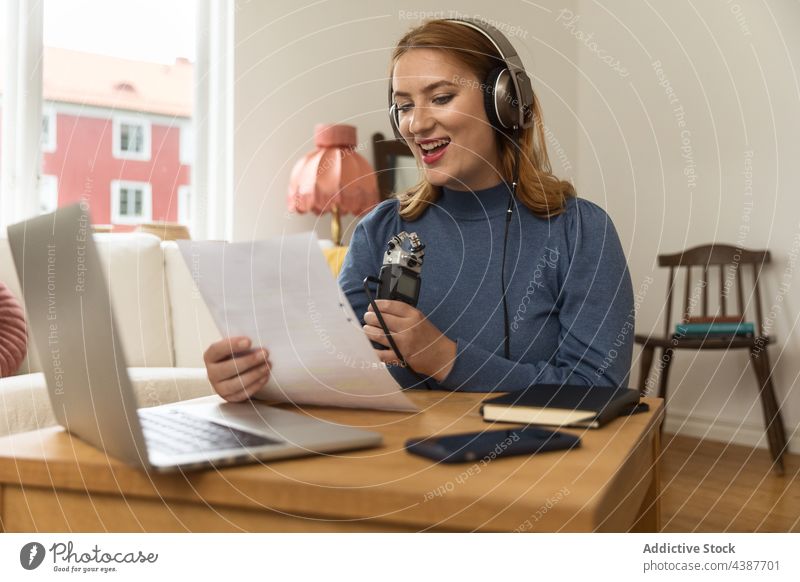 Cheerful woman recording podcast and using microphone speak talk headphones host radio female read note paper broadcast smile cheerful delight content home